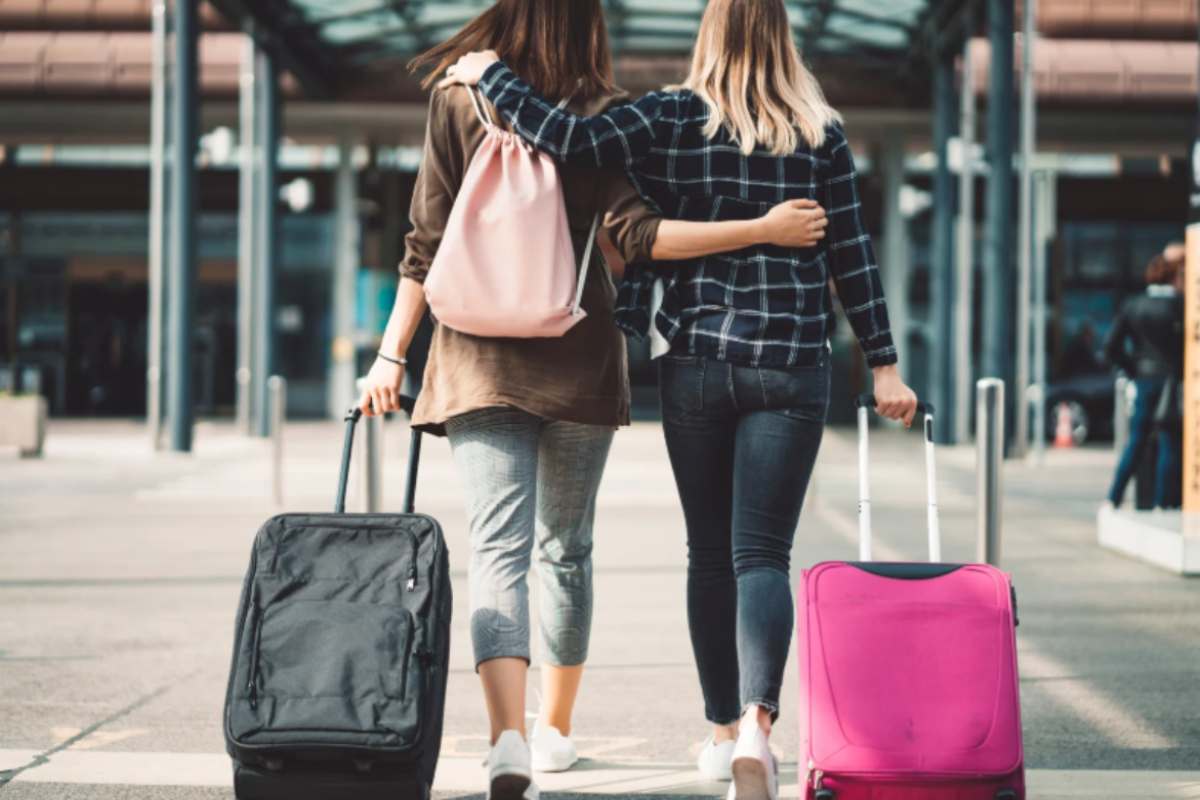 due ragazze di spalle con le valigie che vanno verso l'aeroporto