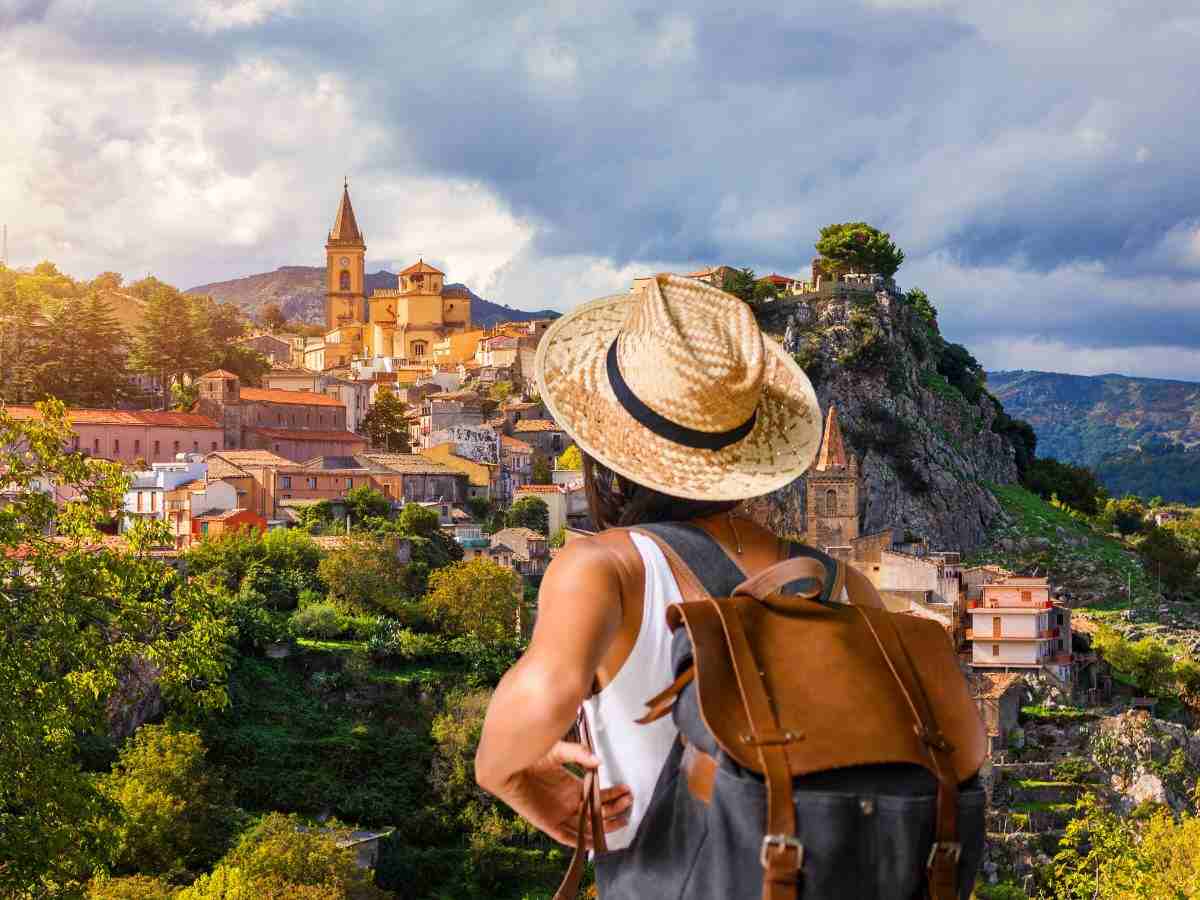 sfondo paese su promontorio e donna di spalle con zaino