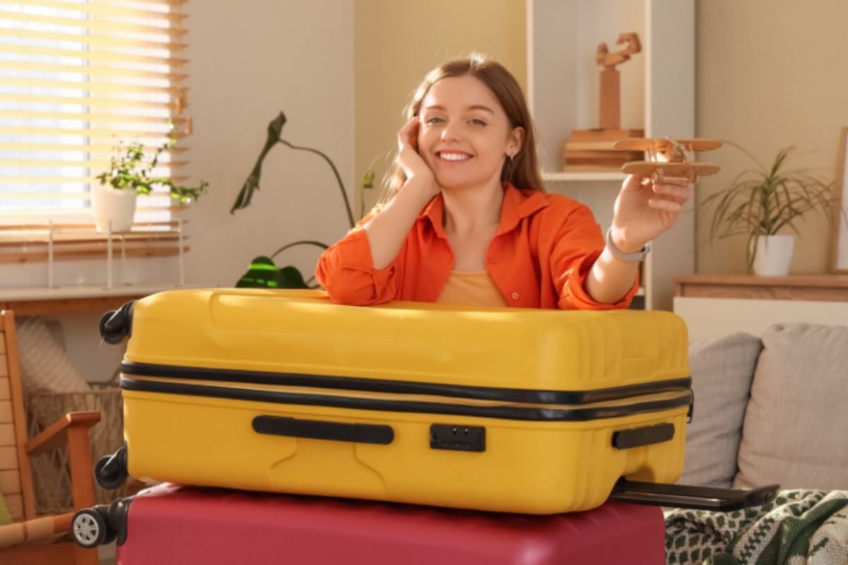 donna appoggiata sulla valigia con un aeroplanino in mano