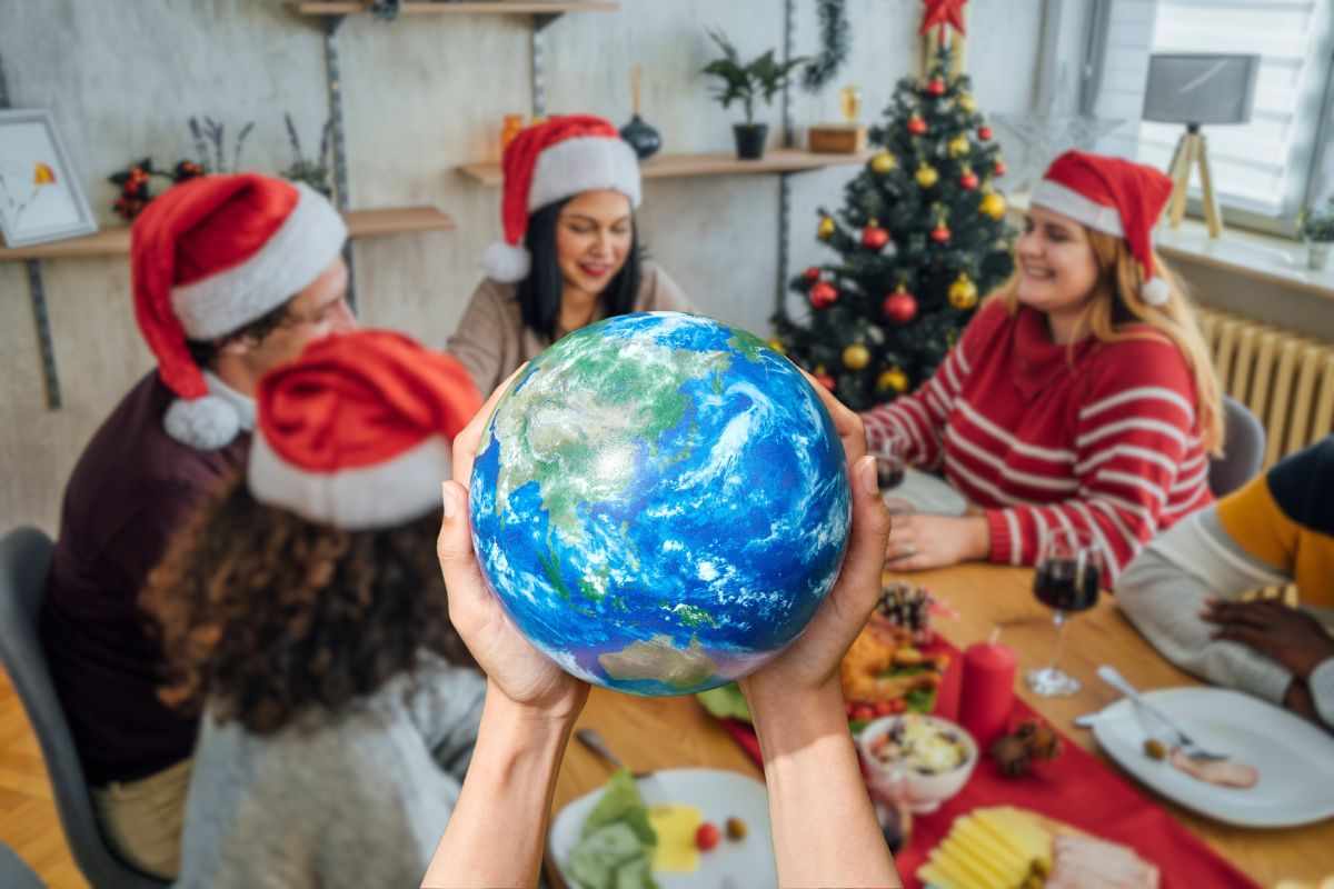 persone sedute a tavola per natale e mani che sostengo la terra