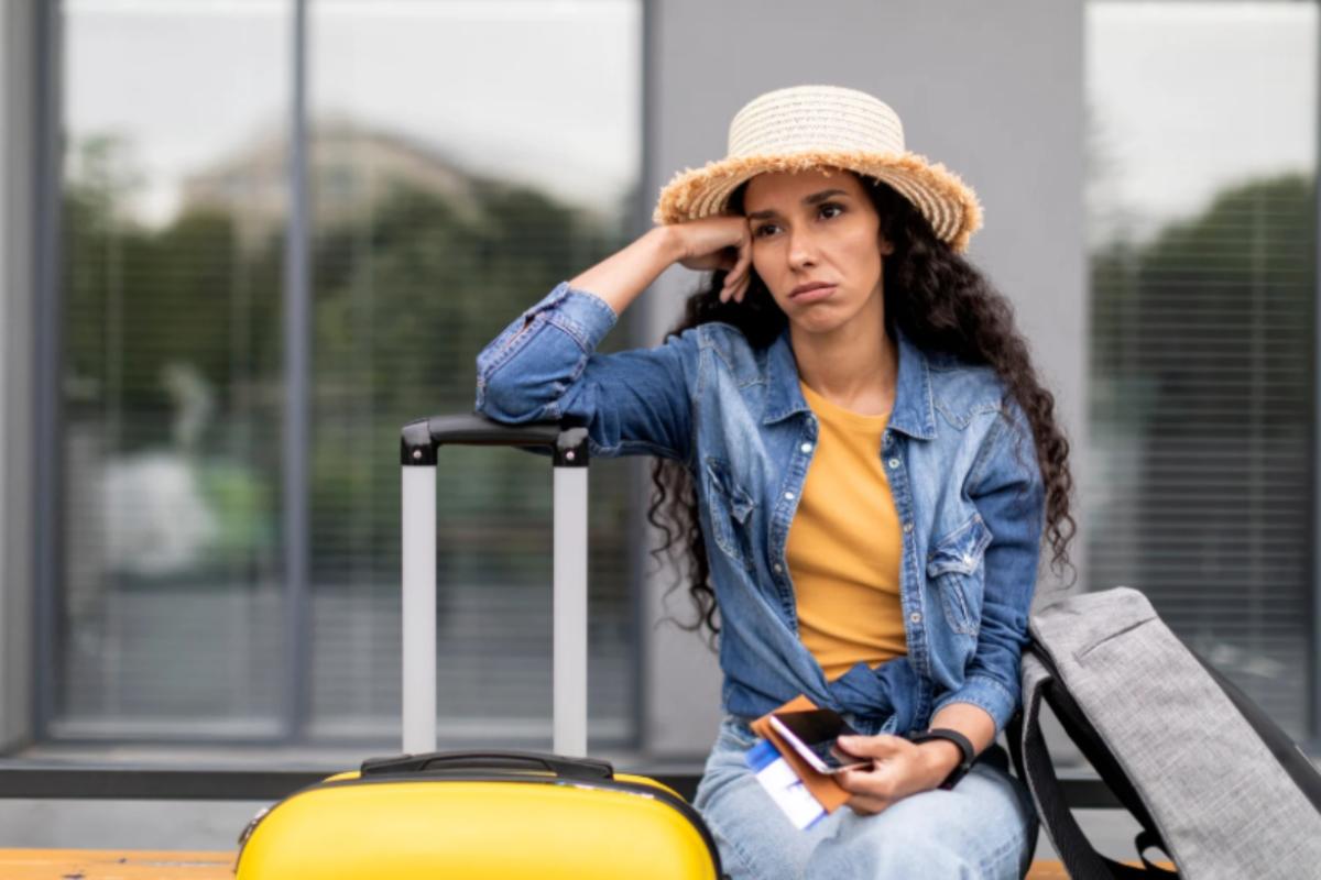 donna triste con accanto un trolley e uno zaino