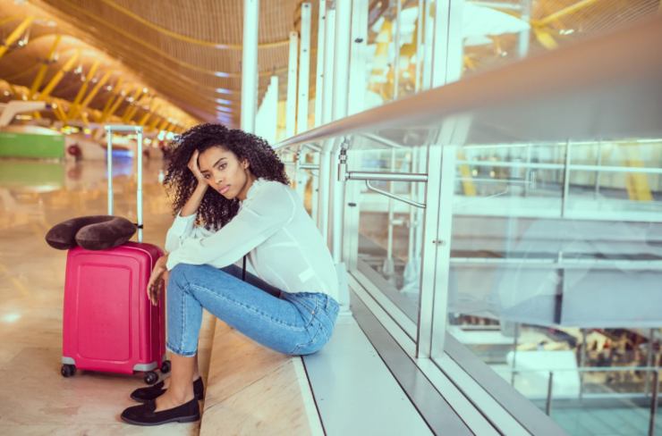 donna triste seduta per terra in aeroporto con accanto un trolley