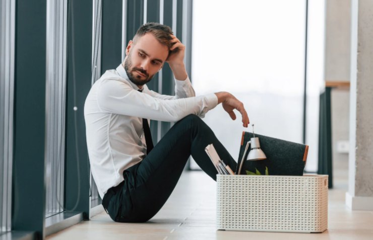 uomo seduto per terra fuori da un ufficio con accanto uno scatolone