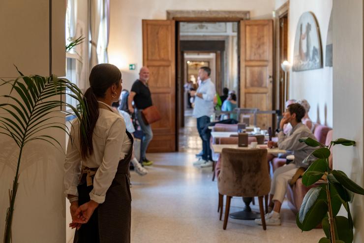 Persone che fanno aperitivo al bar del Museo Palazzo Reale Correr. Cameriera di schiena in primo piano